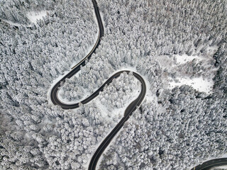 Winding road aerial view by drone. Brasov, Romania. There are huge snow mountains and long winding road in this area. This is a great place to drive and stop during a road trip.
