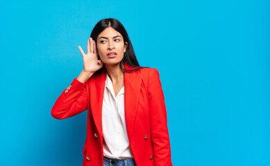 young hispanic businesswoman looking serious and curious, listening, trying to hear a secret...