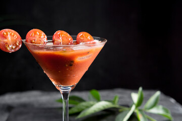 Sopa de tomate fría española, gazpacho, hecha con tomate, pepino, pimiento, cebolla, ajo y aceite de oliva servida en copa de cóctel con tomates cherry sobre fondo negro