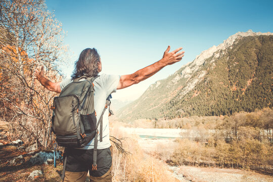 A man with a backpack against the background of blue sky and mountains. He spread his arms wide and looks ahead. Autumn. back view.
