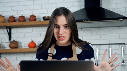 Close up emotional angry woman housewife in apron tells chef teacher online remote video call conference chat laptop in home kitchen. Beautiful female study distance education food course computer