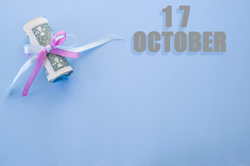 calendar date on blue background with rolled up dollar bills pinned by blue and pink ribbon with copy space.  October 17 is the seventeenth day of the month