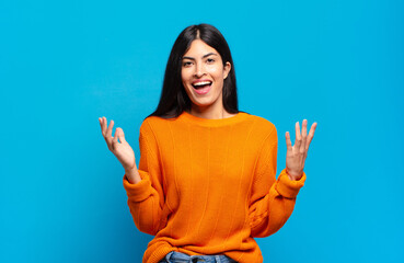 young pretty hispanic woman feeling happy, excited, surprised or shocked, smiling and astonished at...