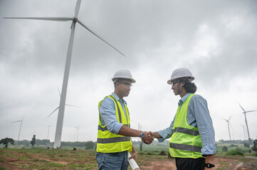 Two engineers working and holding the report at wind turbine farm Power Generator Station on mountain,Thailand people