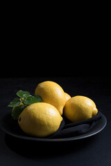 Limones en un plato negro sobre fondo negro