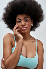 Portrait of voluptuous young woman with afro hair style wearing blue underwear looking at camera, posing isolated over light background