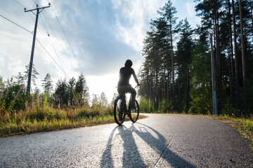A woman rides a bike on a bike path near a pine forest and enjoys a warm summer evening. Healthy lifestyle concept.
