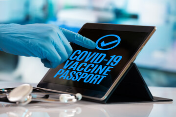Hand of a doctor pressing a button on the tablet that authorizes the Covid-19 digital vaccination passport for a traveling patient. Immunity, vaccination and digital passport concept. Doctor presses
