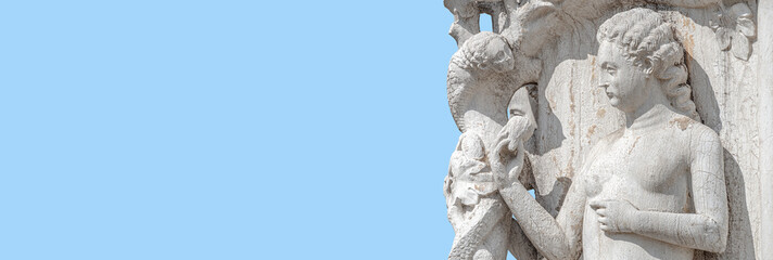 Fototapeta premium Banner with ancient sculpture of beautiful Eva with apple taken from snake, the Bible story, at Doge Palace in Venice, Italy, with copy space and blue sky. Concept art, religion and heritage.