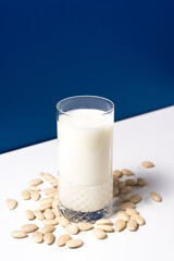 Vaso de leche vegetal de almendras con almendras naturales blancas sobre mesa blanca y fondo azul
