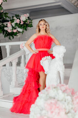 Fototapeta premium A young blonde woman in a beautiful puffy pink dress. A beautiful woman in a light-colored photo studio. Ball Gown. Portrait of a girl with makeup and hairstyle