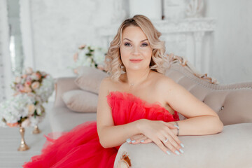 Naklejka premium A young blonde woman in a beautiful puffy pink dress. A beautiful woman in a light-colored photo studio. Ball Gown. Portrait of a girl with makeup and hairstyle