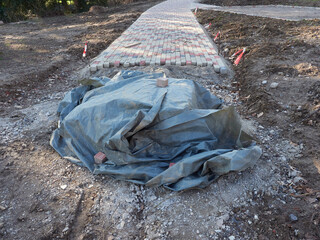 Unfinished pavement construction. A pile of paving stones covered with a foil sheet. Construction of a paved path in the park.