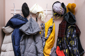 Many winter coats and caps, hats hanging in a mess on hooks in a corridor, decluttering warm clothes