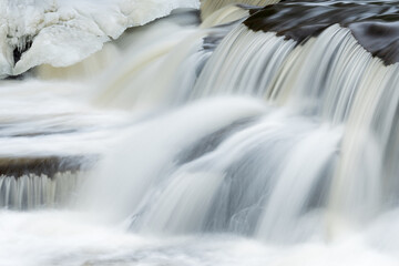 Winter landscape of a cascade at Bond Falls captured with motion blur and framed by ice and snow, Michigan's Upper Peninsula, USA