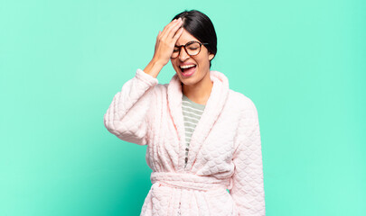 young pretty woman laughing and slapping forehead like saying d’oh! I forgot or that was a stupid...