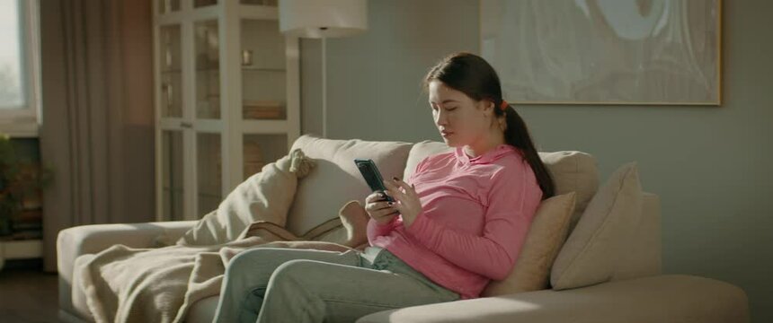 WIDE Portrait of Asian Korean female checking her phone at home early in the morning. Natural cinematic light. Shot with 2x anamorphic lens