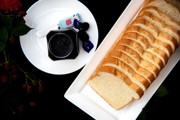 Sliced Bread Loaf on White Plate with  a Glass Jar of Homemade Blackberry Jam on Black Background