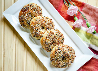 Homemade Everything Bagels on White Plate on Wood Background; Flatlay