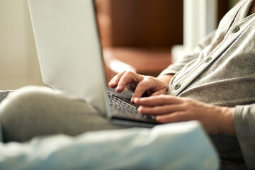  A fragment of an adult man at a laptop in bed. Selective focus.