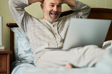 Fototapeta premium Sports fan in bed with a laptop. He reacts emotionally to a sports Internet broadcast. Selective focus.
