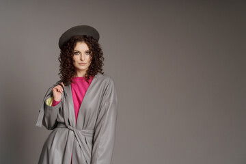 Fototapeta premium Studio shot of curly fashion model in bright pink clothes and leather jacket on gray background with copy space