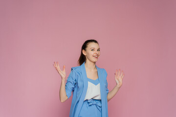A shoked woman is shruging. A woman is open-eyes on the pink background