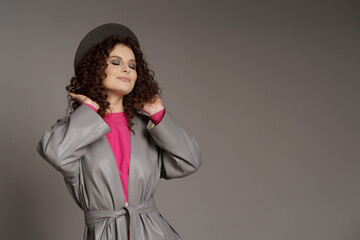 Studio shot of curly fashion model in bright pink clothes and leather jacket on gray background with copy space