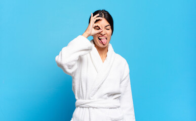 young hispanic woman smiling happily with funny face, joking and looking through peephole, spying...