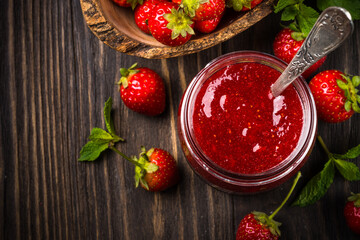 Strawberry jam in the glass jar with fresh berries at wooden table. Top view image with copy space.