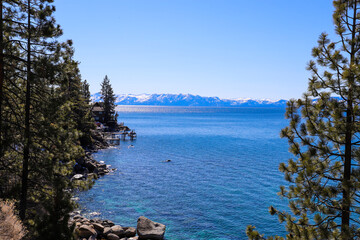 a gorgeous winter landscape with clear blue lake water, snow capped mountain ranges and lush green...