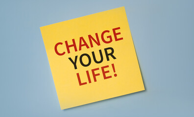 Yellow reminder sticky note on a blue wall with CHANGE YOUR LIFE text. Motivation concept.