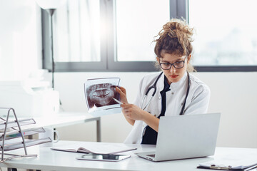 Young female doctor shows patient magnetic resonance image on video call. Young female doctor shows...