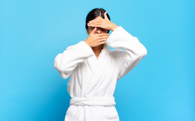 young hispanic woman covering face with both hands saying no to the camera! refusing pictures or...