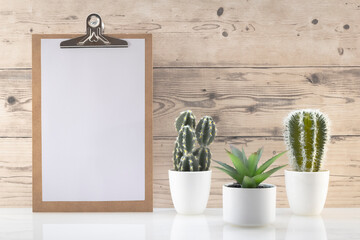 Modèle de planchette à pince en bois avec espace vide pour logos, inscription publicitaire. Feuille blanche dans un cadre en mode portrait sur un espace de travail avec des plantes vertes.