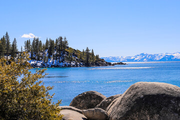 a stunning shot of the vast clear blue lake water with snow capped mountain ranges and lush green...