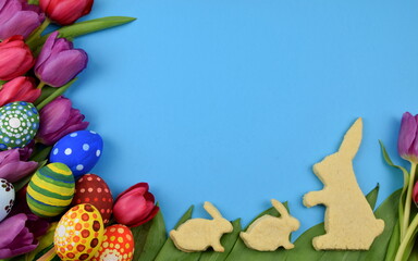 tulips, painted eggs and bunny shaped cookies on blue background