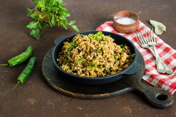 Dirty rice, Cajun cuisine dish, rice with liver, minced pork, aubergine , green pepper and spices in a cast iron skillet on a brown concrete background.