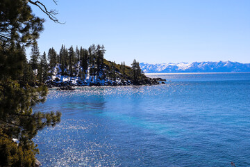  a stunning shot of the vast clear blue lake water with snow capped mountain ranges and lush green...