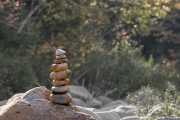Fototapeta na wymiar Zen stones balanced on top of bigger rock with foliage behind