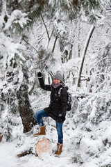 Smiling young woman standing on fallen tree after sleet load and snow in a snow-covered winter park. Girl enjoying snowy winter, frosty day. Walk in winter forest