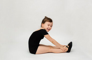 Fototapeta premium joyful little gymnast girl sits sideways and does a stretch on a white background with space for text