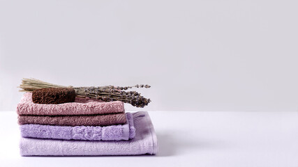 Fototapeta na wymiar Stack soft, cotton towels, purple shades, lavender and foot peeling on a light background, selective focus, copying space.