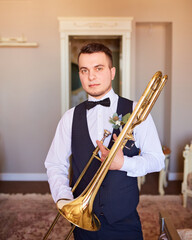 Young groom professional trumpeter holding a trumpet in his hands.