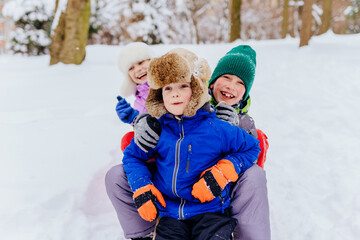 Group portrait of three happy children in winter clothes laughing, embracing while playing in a snowy park, outside.