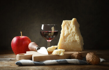 Parmigiano Reggiano with cutting board, knife and fork on wooden table. Rustic snack.