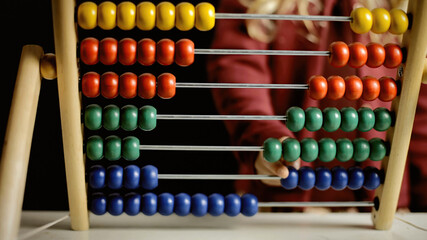 A little girl playing with an abacus, learning to count. Front view, detail of the beads and of the hand shifting them.
