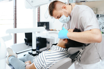 Fototapeta premium Smiling young man sitting in dentist chair while doctor examining his teeth