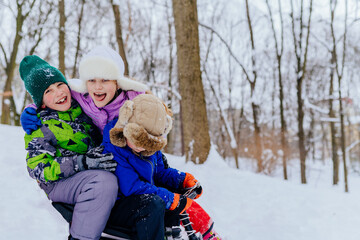 Fototapeta premium Childhood, leisure and season concept. Group of three happy laughing little kids in winter clothes playing outdoors in winter park.