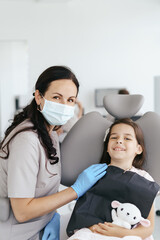 Cute little girl sitting on a modern dental chair and having dental consultation with dentist